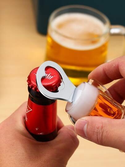 Close-up of hands using a metal bottle opener to pry the red cap off a small orange bottle, with a glass of beer blurred in the background. - Bling On Decor® | Luxury Handmade Home Decor ANJU BALA