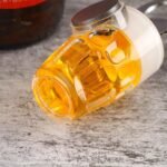 17242105680c0ab67e6906e70fa8f35848c613b01e.jpg - Bling On Decor® | Luxury Handmade Home Decor Close-up of a clear glass bottle with orange liquid and a black cap on a textured wooden surface. - Bling On Decor® | Luxury Handmade Home Decor ANJU BALA