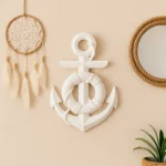 Nautical wall decor: a white anchor sculpture centered between a dreamcatcher on the left and a rope-framed round mirror on the right, with a potted plant in the bottom corner against a beige wall. - Bling On Decor® | Luxury Handmade Home Decor ANJU BALA