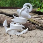 White anchor-shaped plastic object with a braided rope wrapped around it, resting on sandy ground near a piece of driftwood. - Bling On Decor® | Luxury Handmade Home Decor ANJU BALA