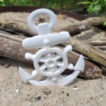 White plastic toy ship's wheel and anchor resting on sandy beach with driftwood in the background - Bling On Decor® | Luxury Handmade Home Decor ANJU BALA