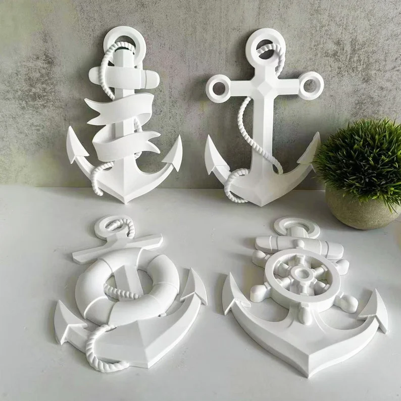 Set of white decorative nautical anchors and rope-wrapped pieces on a white table, against a gray wall with a small potted plant nearby. - Bling On Decor® | Luxury Handmade Home Decor ANJU BALA