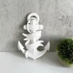 White decorative anchor sculpture with a ribbon wrapped around it, sitting on a light surface beside a small green plant. - Bling On Decor® | Luxury Handmade Home Decor ANJU BALA
