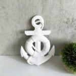 White decorative anchor sculpture with coiled rope, placed on a light gray wall beside a small green plant. - Bling On Decor® | Luxury Handmade Home Decor ANJU BALA