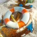 Colorful beach-themed ornament in white sand: an orange-and-white lifebuoy with shells and a glittery brown starfish piece. - Bling On Decor® | Luxury Handmade Home Decor ANJU BALA