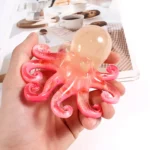 Pink translucent octopus toy held in a hand, with a table of cookies and coffee blurred in the background. - Bling On Decor® | Luxury Handmade Home Decor ANJU BALA