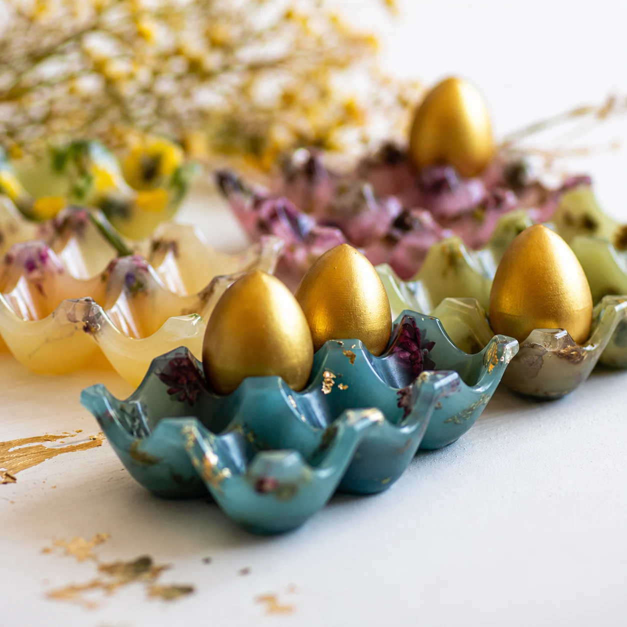 Decorative gold and colorful foil Easter eggs arranged in blue and teal egg cups on a white surface. - Bling On Decor® | Luxury Handmade Home Decor ANJU BALA
