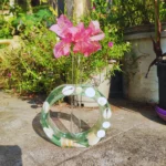 Pink bougainvillea bouquet in a tall glass vase on a shell-decorated circular stand outdoors, with greenery in the background. - Bling On Decor® | Luxury Handmade Home Decor ANJU BALA