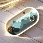 Decorative oval tray with blue wave design holding gold rings and a pearl bracelet on a light wooden surface - Bling On Decor® | Luxury Handmade Home Decor ANJU BALA