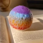 Rainbow-colored spherical object resting on an open book, showing purple, blue, orange to red gradient. - Bling On Decor® | Luxury Handmade Home Decor ANJU BALA