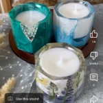 Three decorative scented candles in glass holders on a round wooden tray, set on a patterned tablecloth. - Bling On Decor® | Luxury Handmade Home Decor ANJU BALA