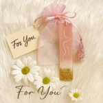 Bling-On®-Resin-Coaster-Bookmark-Set-of-2-Luxe-Gold-Feminine-Edition-.webp - Bling On Decor® | Luxury Handmade Home Decor Pink gift tag and sheer pink pouch with a tassel on a fluffy white surface, with daisies and 'For You' cards nearby. - Bling On Decor® | Luxury Handmade Home Decor ANJU BALA