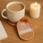 Cream mug of coffee on a wooden table beside a lit pillar candle and a pink decorative card with a line-drawn woman and a glittery gold base - Bling On Decor® | Luxury Handmade Home Decor ANJU BALA