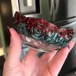 Close-up of a hand holding a glossy red-and-teal iridescent object, possibly jewelry or decorative piece, with a blurred kitchen-like background. - Bling On Decor® | Luxury Handmade Home Decor ANJU BALA