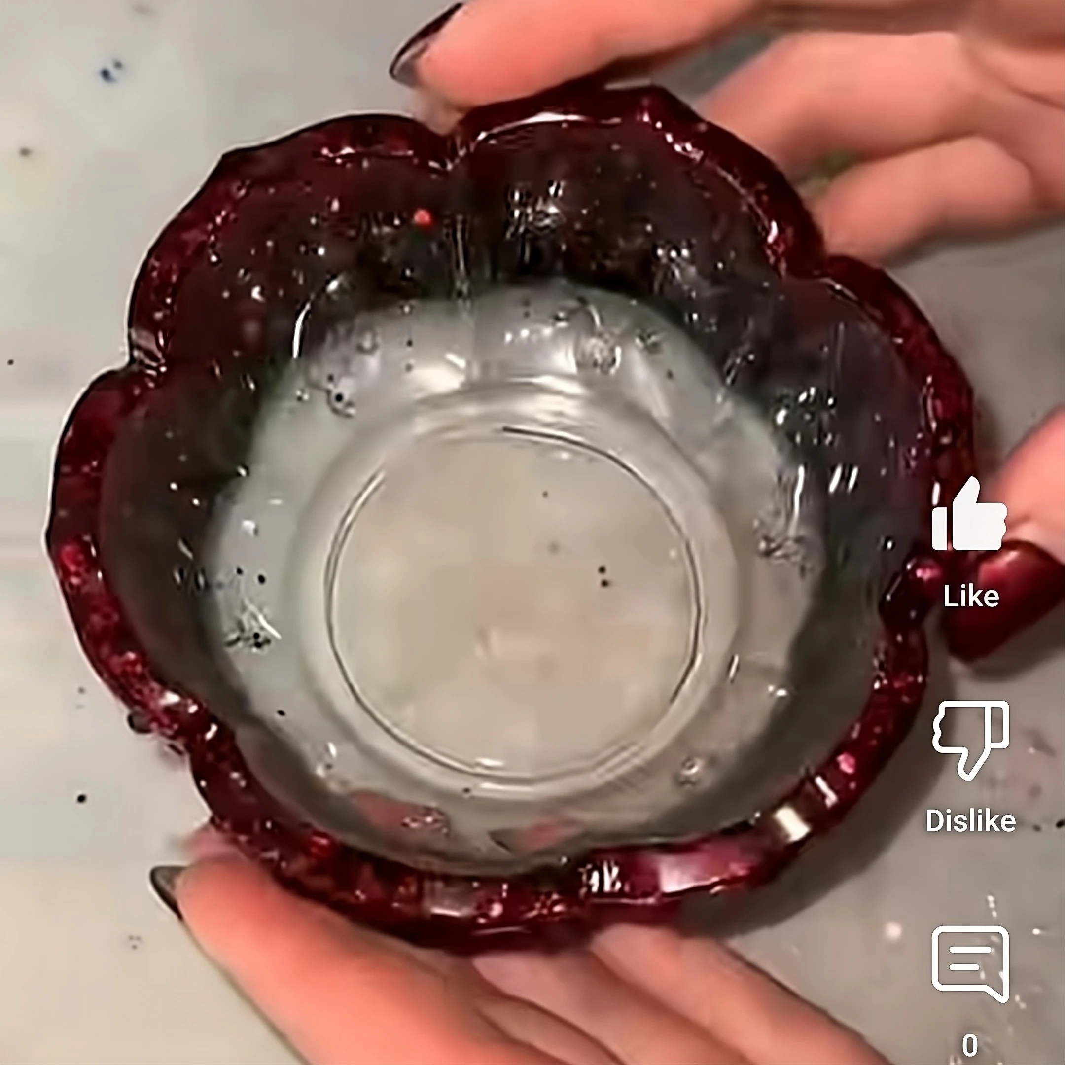 Close-up of a small glass orb held between fingers with a red, jagged ring around its edge; onscreen like/dislike icons are visible in the frame. - Bling On Decor® | Luxury Handmade Home Decor ANJU BALA