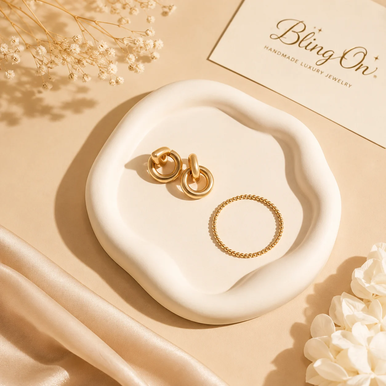Gold jewelry set on a white ceramic dish: two hoop earrings and a beaded ring, with a BlingOn card in the background and soft beige decor. - Bling On Decor® | Luxury Handmade Home Decor ANJU BALA