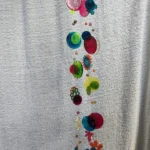 Vertical garland of colorful translucent discs and plastic flowers hanging against a textured towel backdrop. - Bling On Decor® | Luxury Handmade Home Decor ANJU BALA
