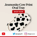 Advertisement for a Jesmonite cow-print oval tray with a red 'Shop Now' button, angled tray on a light background. - Bling On Decor® | Luxury Handmade Home Decor ANJU BALA