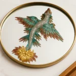 Round gold-framed circular mirror reflecting a multicolored phoenix sculpture perched on a golden flower base. - Bling On Decor® | Luxury Handmade Home Decor ANJU BALA
