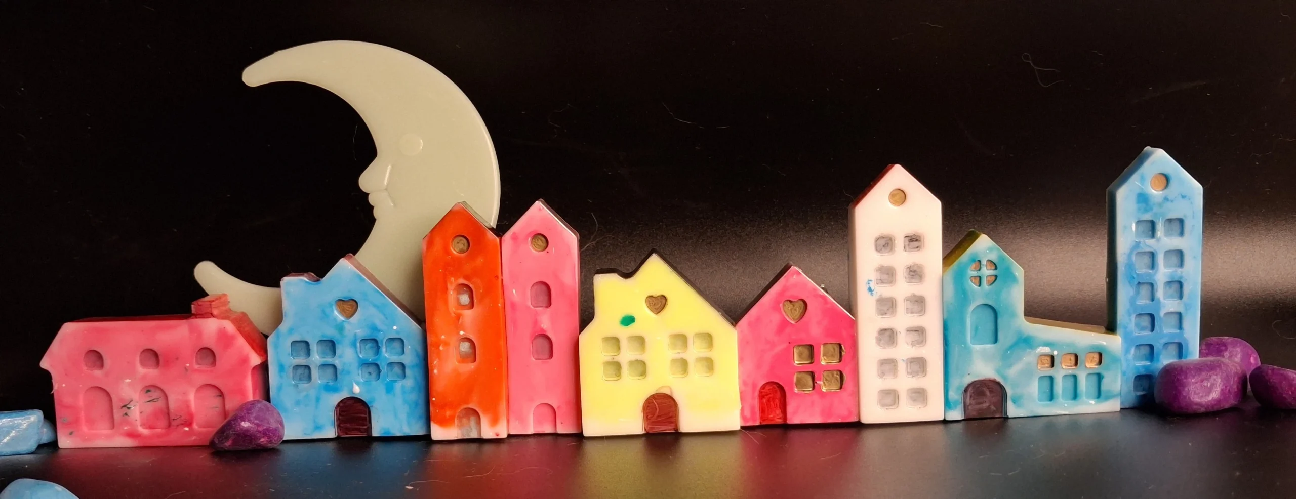 Whimsical row of colorful ceramic houses with a large white crescent moon sculpture behind them on a dark background. - Bling On Decor® | Luxury Handmade Home Decor ANJU BALA