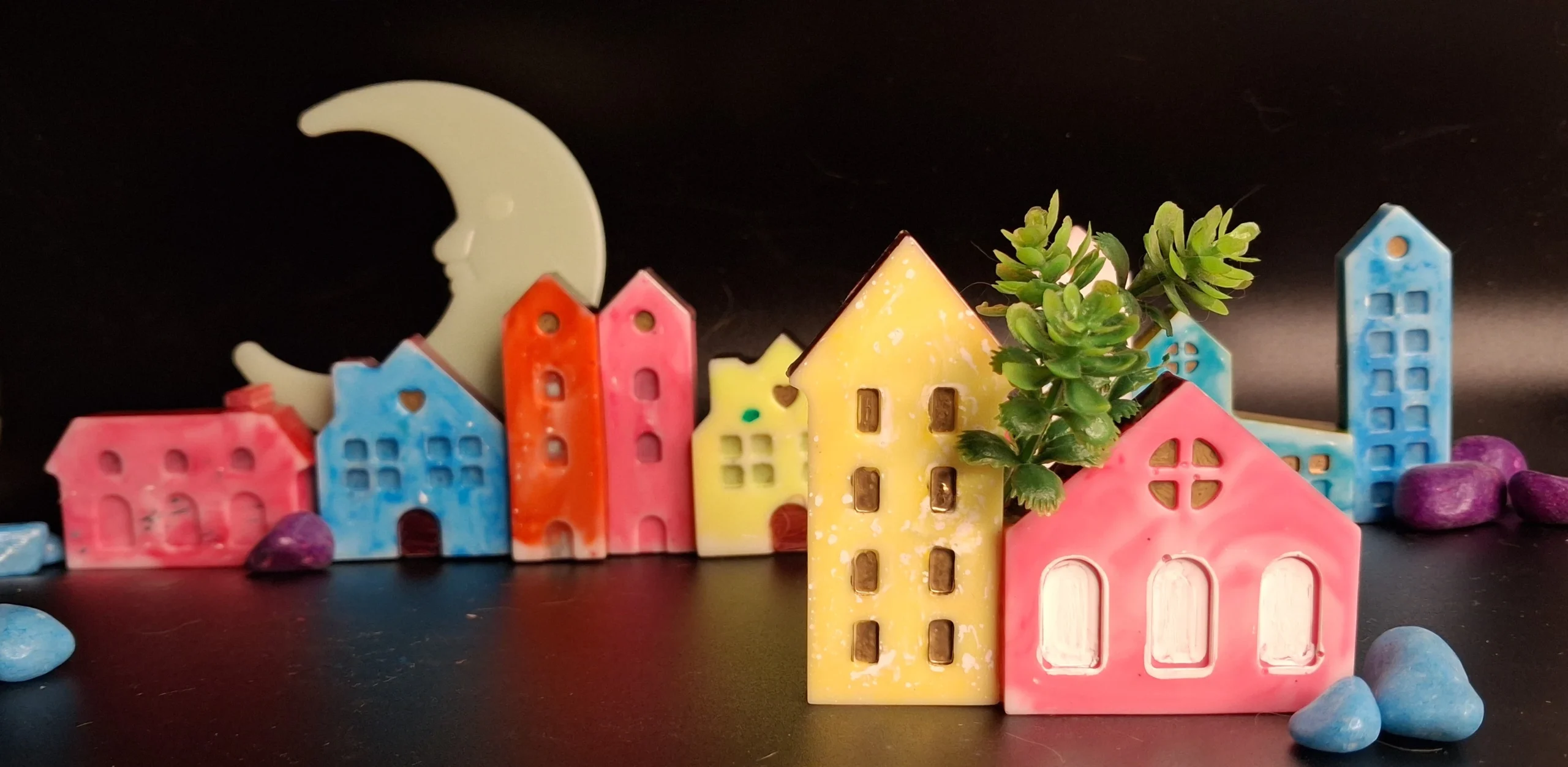 Colorful ceramic town figurines arranged in a row with a large pale crescent moon in the dark background; whimsical decorative scene. - Bling On Decor® | Luxury Handmade Home Decor ANJU BALA
