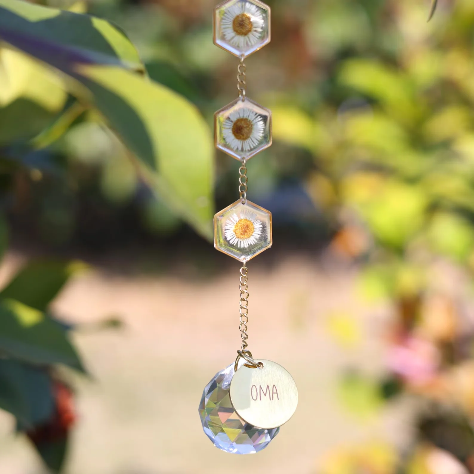 Wind chime with hexagonal glass beads showing daisies, hanging on a chain against a sunlit garden background. - Bling On Decor® | Luxury Handmade Home Decor ANJU BALA