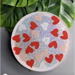 Plate covered with holographic glitter and red/pastel heart shapes, set on a table with green leaves in the background. - Bling On Decor® | Luxury Handmade Home Decor ANJU BALA