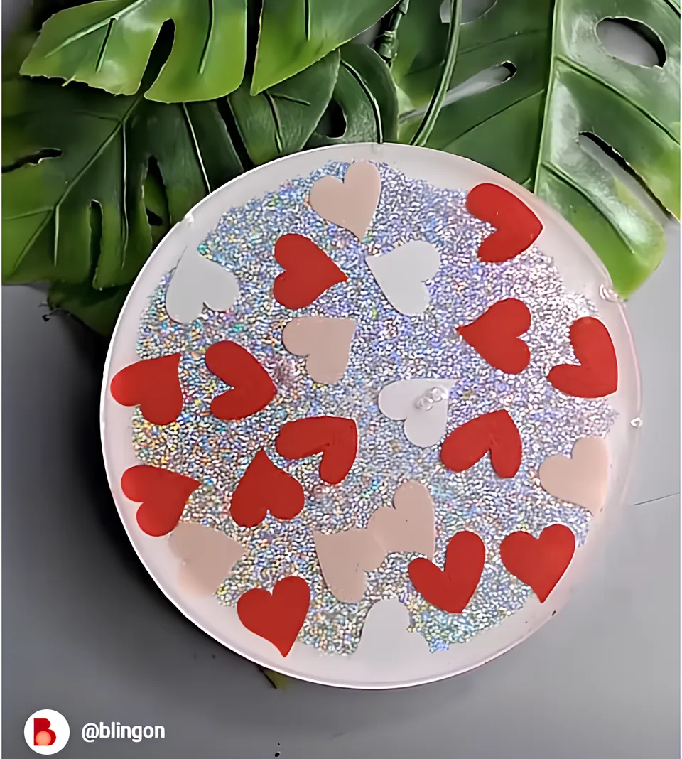 Plate covered with holographic glitter and red/pastel heart shapes, set on a table with green leaves in the background. - Bling On Decor® | Luxury Handmade Home Decor ANJU BALA