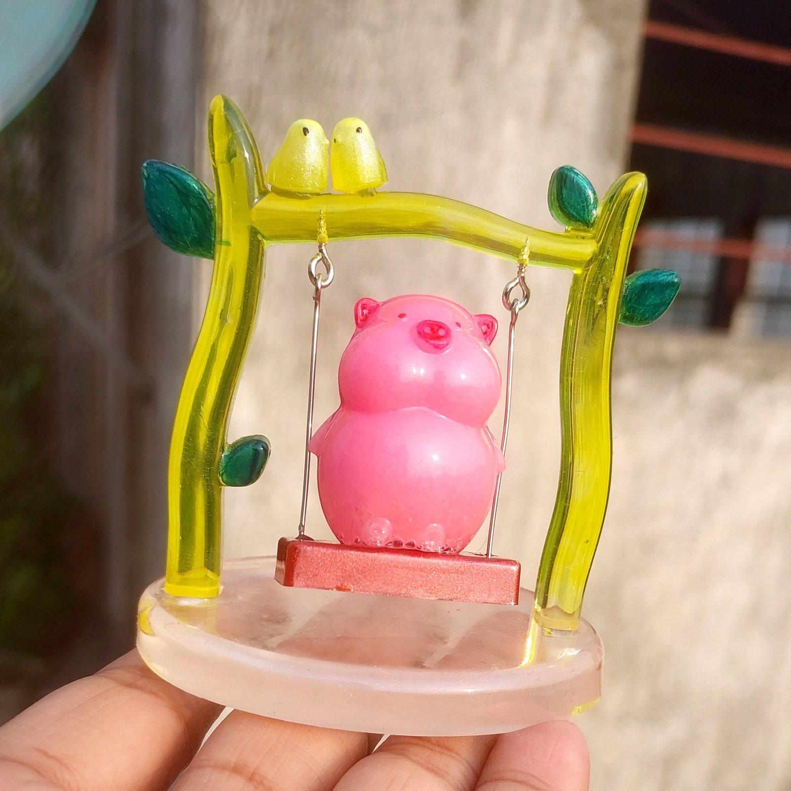 Pink pig figurine hanging inside a translucent yellow-green frame with small metal chains, atop a circular base (ornamental display). - Bling On Decor® | Luxury Handmade Home Decor ANJU BALA