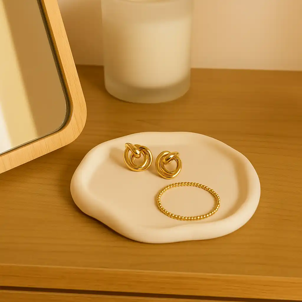 Two gold-tone hoop earrings with a matching small beaded bracelet placed on a white ceramic dish on a wooden surface next to a mirror. - Bling On Decor® | Luxury Handmade Home Decor ANJU BALA