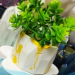 Close-up of bright green herb sprigs in a white container with yellow paint marks on a blue surface behind them. - Bling On Decor® | Luxury Handmade Home Decor ANJU BALA