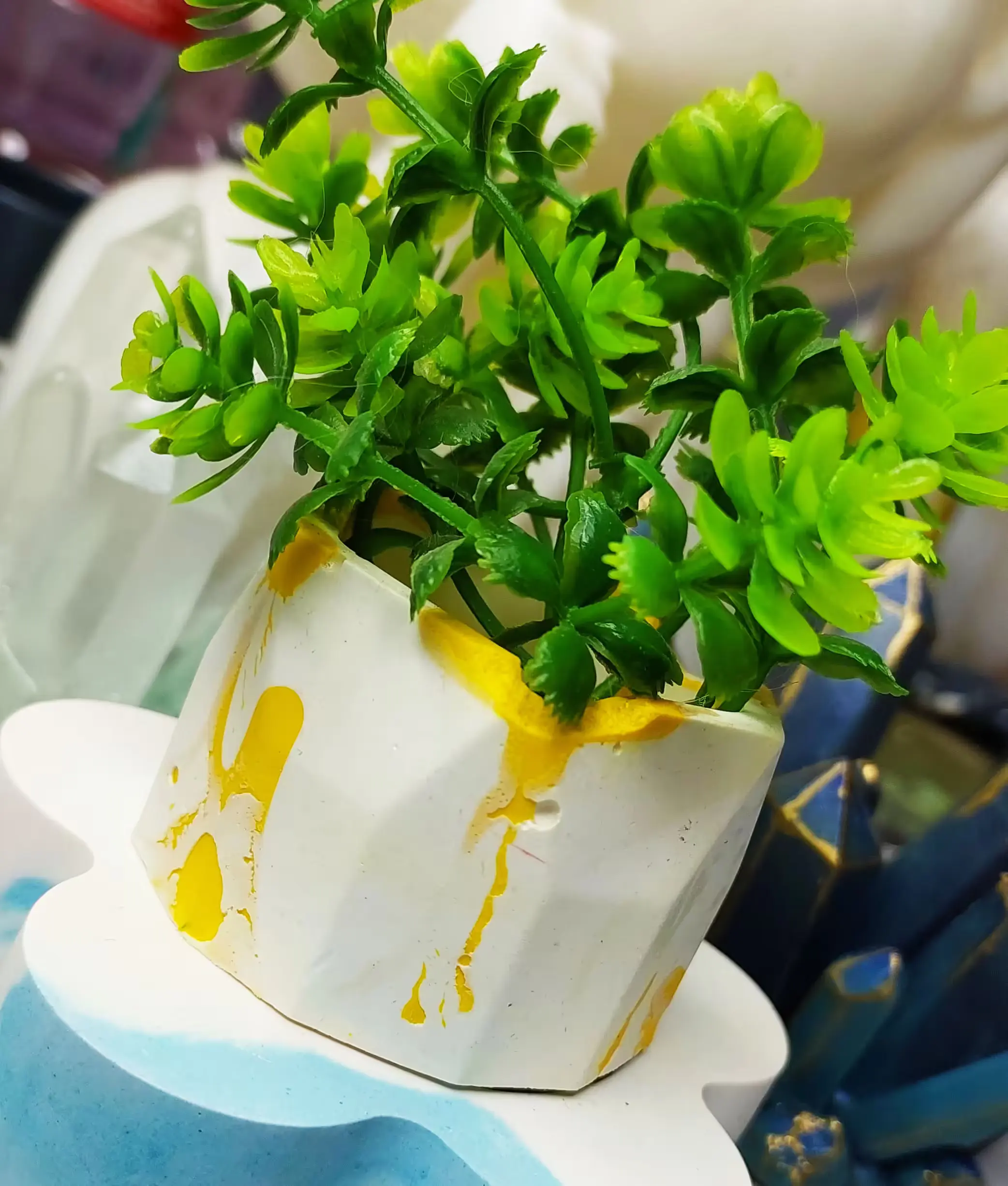 Close-up of a small green herb plant with bright, glossy leaves in a white container stained with yellow paint. - Bling On Decor® | Luxury Handmade Home Decor ANJU BALA