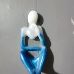 Top-down view of a small porcelain figurine shaped like a person with a white head and a glittery blue dress on a gray surface. - Bling On Decor® | Luxury Handmade Home Decor ANJU BALA