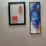 Modern-Abstract-3D-Face-Wall-Art-Frame-Handmade-Resin-Sculpture-Minimalist-Luxury-Home-Decor-by-Bling-On®-India-🇮🇳-1-scaled-1.webp - Bling On Decor® | Luxury Handmade Home Decor Left: pink abstract face sculptures mounted in a black frame on a light wall; right: tall blue Buddha poster framed in black against the wall - Bling On Decor® | Luxury Handmade Home Decor ANJU BALA