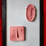 Modern-Abstract-3D-Face-Wall-Art-Frame-Handmade-Resin-Sculpture-Minimalist-Luxury-Home-Decor-by-Bling-On®-India-🇮🇳-4-scaled-1.webp - Bling On Decor® | Luxury Handmade Home Decor Pink clay sculpture of a stylized face with an elongated nose, set inside a black picture frame on a white mat with a red background. - Bling On Decor® | Luxury Handmade Home Decor ANJU BALA