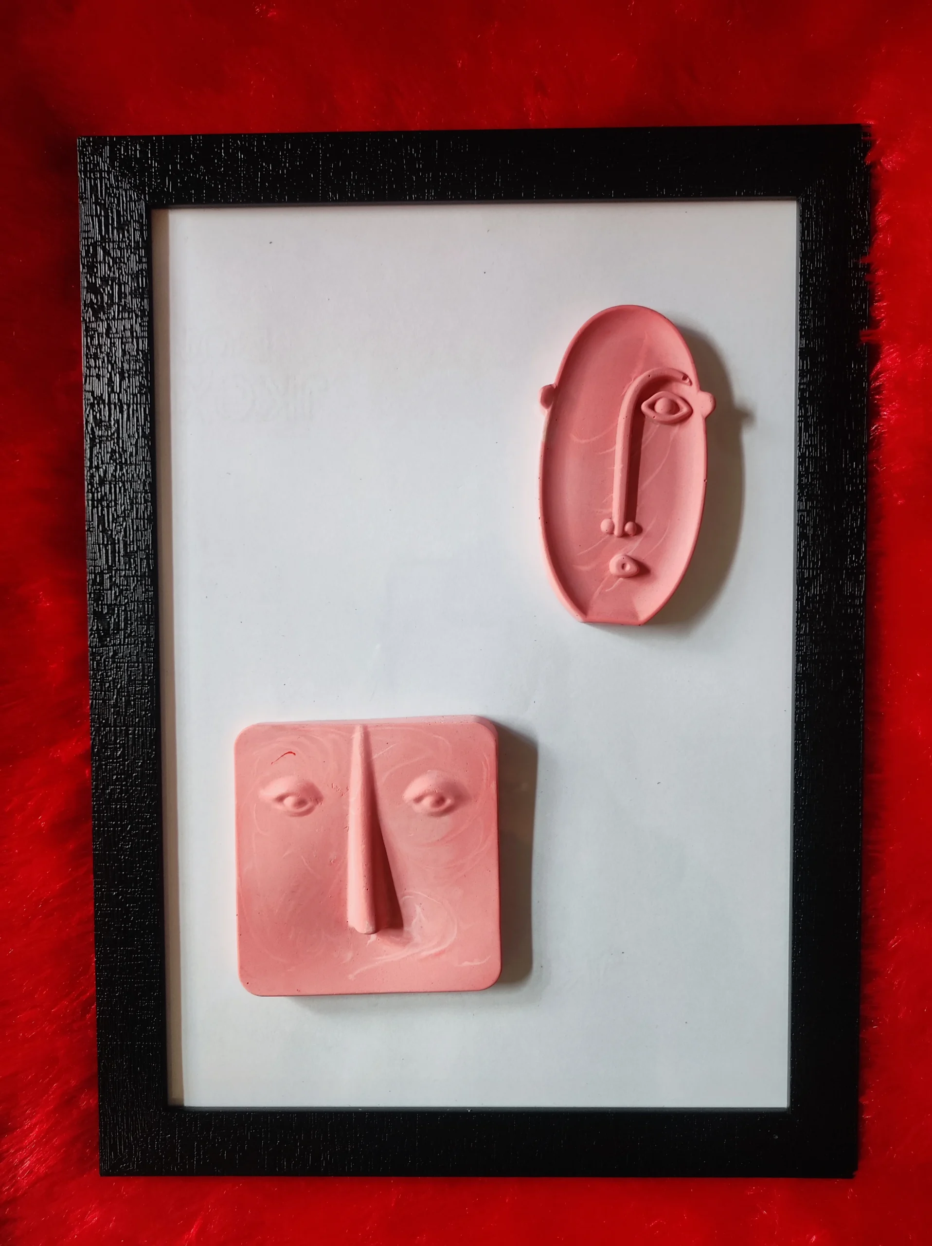 Modern-Abstract-3D-Face-Wall-Art-Frame-Handmade-Resin-Sculpture-Minimalist-Luxury-Home-Decor-by-Bling-On®-India-🇮🇳-5-scaled-1.webp - Bling On Decor® | Luxury Handmade Home Decor Pink clay sculptures of faces mounted on a white background inside a black frame, set on red fuzzy fabric. - Bling On Decor® | Luxury Handmade Home Decor ANJU BALA