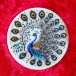 Round ceramic plate with a painted peacock and ornate tail feathers on a bright red textured background on velvet-like fabric. - Bling On Decor® | Luxury Handmade Home Decor ANJU BALA