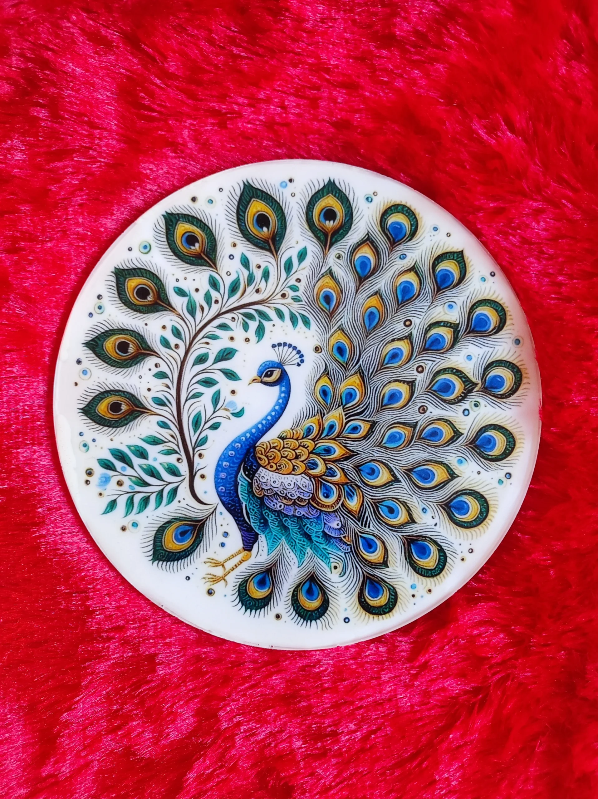 Round ceramic plate with a painted peacock and ornate tail feathers on a bright red textured background on velvet-like fabric. - Bling On Decor® | Luxury Handmade Home Decor ANJU BALA