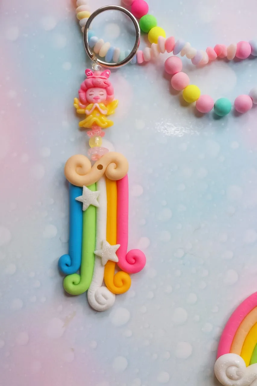 Colorful clay keychain with rainbow strands, stars, and a pink fairy figure on top; hangs from a pastel beaded chain. - Bling On Decor® | Luxury Handmade Home Decor ANJU BALA