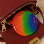 Round rainbow gradient resin badge resting on a red leather handbag with a gold zipper. - Bling On Decor® | Luxury Handmade Home Decor ANJU BALA