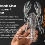 Close-up of a clear resin lobster held by fingers, with an orange resin lobster to the right and bold white text on a dark background. - Bling On Decor® | Luxury Handmade Home Decor ANJU BALA