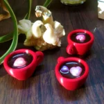 Resin-Love-Cup-table-Top-Desktop-Item-2.webp - Bling On Decor® | Luxury Handmade Home Decor Close-up of small red cups filled with dark liquid and pink spheres, set on a wooden surface with a white coral sculpture nearby. - Bling On Decor® | Luxury Handmade Home Decor ANJU BALA