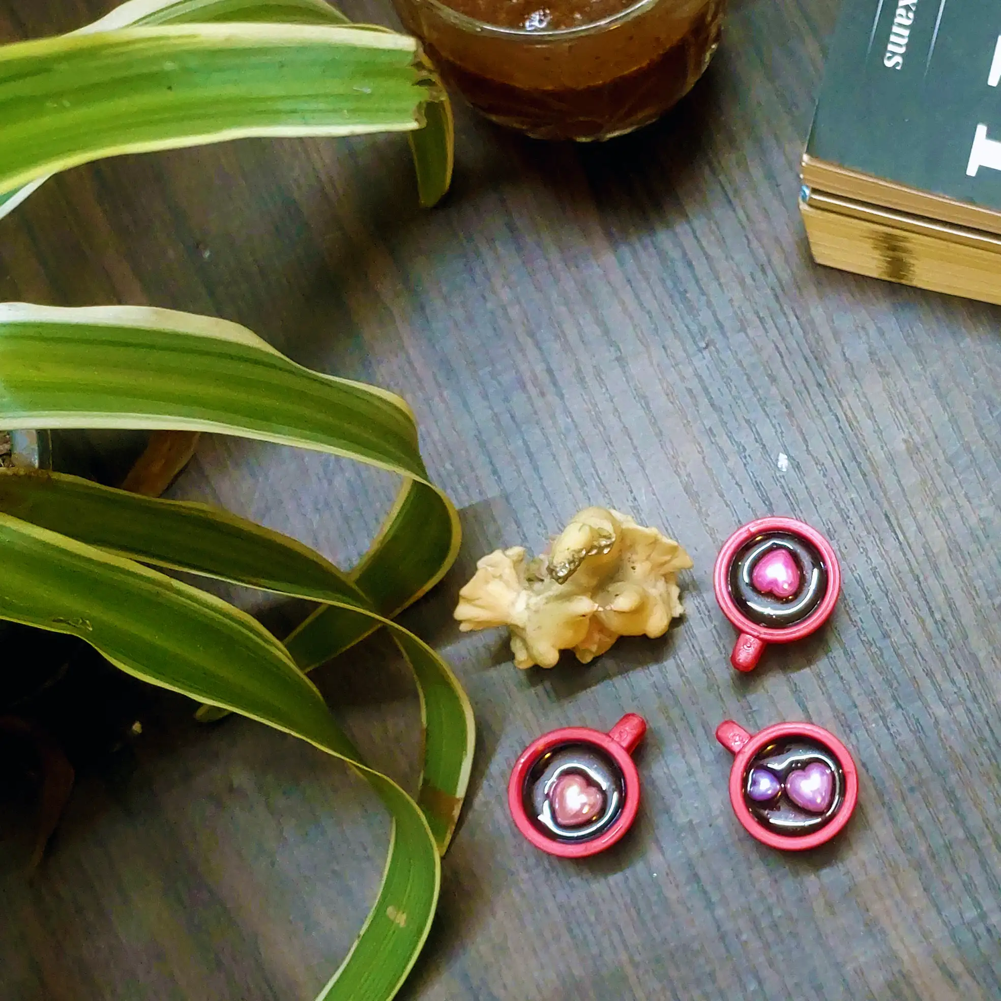 Resin-Love-Cup-table-Top-Desktop-Item-4.webp - Bling On Decor® | Luxury Handmade Home Decor Green variegated plant leaves on a dark wooden surface beside red circular toys with small balls inside (desk scene). - Bling On Decor® | Luxury Handmade Home Decor ANJU BALA