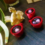 Resin-Love-Cup-table-Top-Desktop-Item-6-scaled-1.webp - Bling On Decor® | Luxury Handmade Home Decor Red round jewelry cases opened to reveal purple beads on a dark wooden surface, with a plant leaf and white coral nearby. - Bling On Decor® | Luxury Handmade Home Decor ANJU BALA