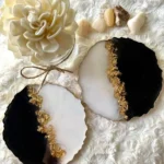 Two black-and-white geode slices with a gold edge sit on a soft white fabric, next to a cream flower and small stones. - Bling On Decor® | Luxury Handmade Home Decor ANJU BALA