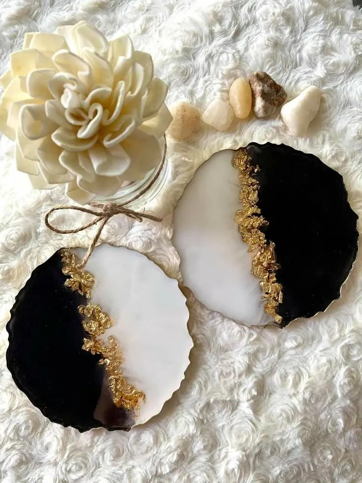 Two black-and-white geode slices with a gold edge sit on a soft white fabric, next to a cream flower and small stones. - Bling On Decor® | Luxury Handmade Home Decor ANJU BALA