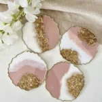 Resin-Pink-Floral-Coaster-Luxury-Handmade-Magic-for-Special-Moments-6-1.webp - Bling On Decor® | Luxury Handmade Home Decor Set of four scalloped-edged coasters featuring pink, white, and gold leaf geode designs on a light surface with white flowers nearby. - Bling On Decor® | Luxury Handmade Home Decor ANJU BALA
