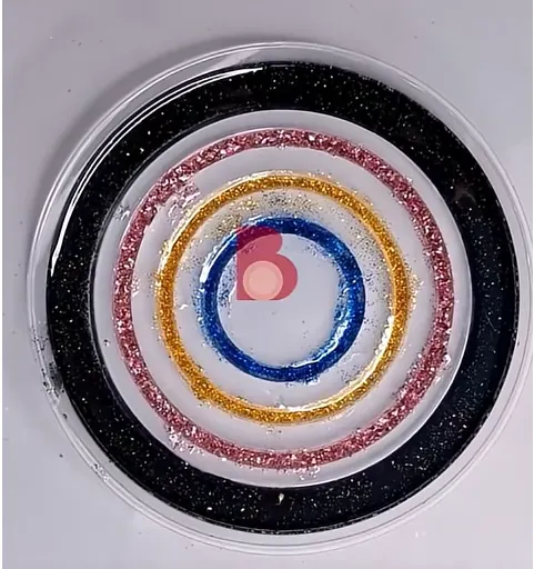 Close-up of a round, clear surface with concentric glitter rings in black, red, gold, blue, and pink, resembling a decorative target. - Bling On Decor® | Luxury Handmade Home Decor ANJU BALA