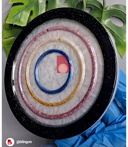 Colorful glittery circular bangles arranged in nested rings on a black plate, blue-gloved hand visible nearby. - Bling On Decor® | Luxury Handmade Home Decor ANJU BALA