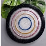 Decorative plate with concentric colored rings (blue center, gold and pink rings) and a black rim, placed on a surface with green leaves in the background. - Bling On Decor® | Luxury Handmade Home Decor ANJU BALA